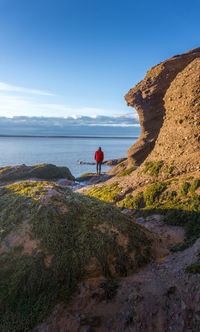 Rear view of man standing on rock formation by sea against sky
