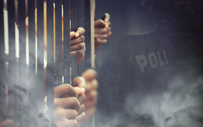 Close-up of prisoner standing behind prison bars
