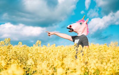 Man with pink unicorn mask gesturing in oilseed rape blooming field