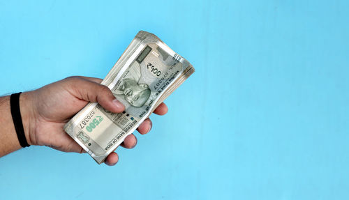 Cropped hand holding paper currency against blue background