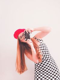 Portrait of young woman photographing with camera against white background