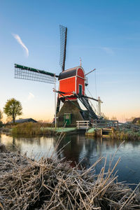 Traditional windmill by river against sky