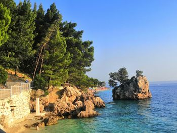 Rocks by sea against clear blue sky