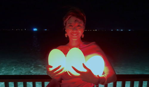 Portrait of woman standing against illuminated lights at night