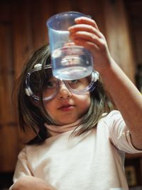 Girl wearing protective eyewear looking at liquid in container at home