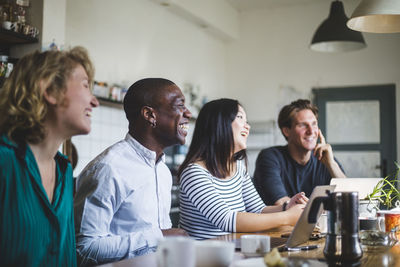 Smiling entrepreneurs sitting while looking away at desk in office