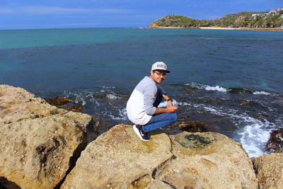 Man standing on rock by sea against sky