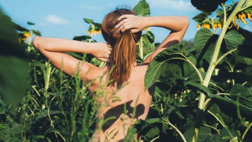 Rear view of topless standing amidst plants