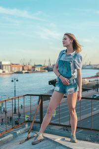 Full length of young woman standing on railing against sky