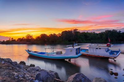 Boats moored on shore against sky during sunset