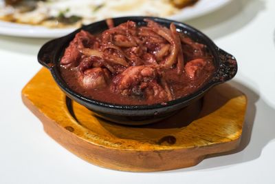 Close-up of meat gravy in utensil on wooden coaster at table