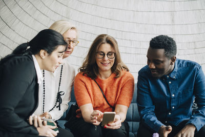 Business professionals looking at mobile phones while sitting on couch against wall