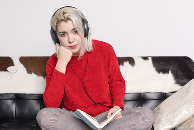 Portrait of young woman using laptop while sitting against wall