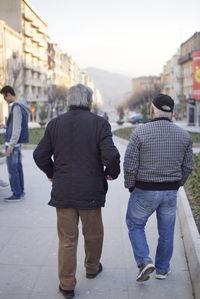 Rear view of men walking on footpath in city