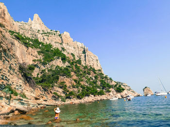 Man on rock by sea against clear sky