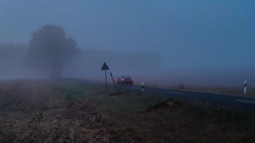 Road amidst field against sky during foggy weather