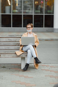 Portrait of beautiful business woman in city with laptop in hands sitting on the bench 