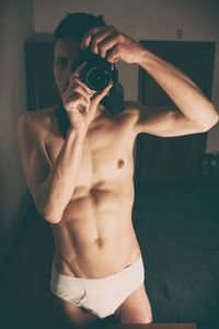 Shirtless young man photographing while standing at home