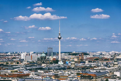 Aerial view of fernsehturm in city against sky during sunny day