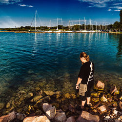 Rear view of man standing on rock by lake against sky