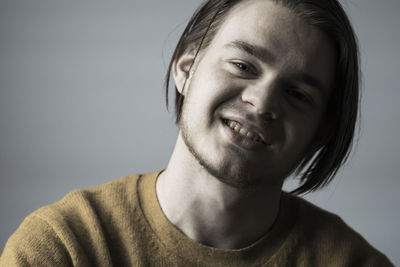 Portrait of smiling young man wearing sweater against gray background