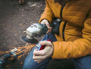 A young caucasian man in a yellow jacket is holding a drill in his hands and polishing a disc