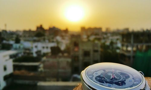 Close-up of clock against cityscape at sunset