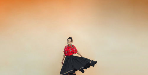 Woman wearing a skirt, dancingagainst orange wall