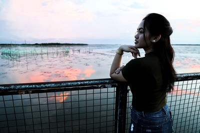 Portrait of young woman standing by railing against sea