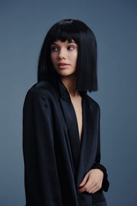 Portrait of young woman standing against blue background