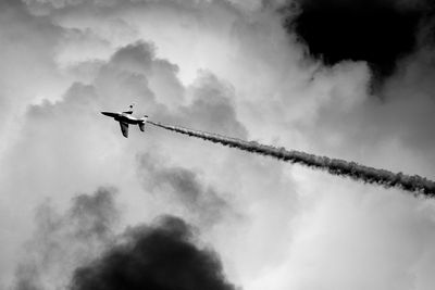 Silhouette aerobatic jet airplane flying between clouds with white smoke