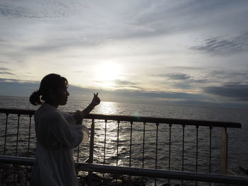 Man standing by railing against sea during sunset
