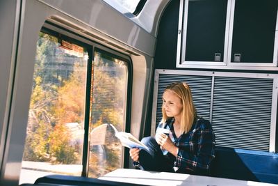 Woman looking at camera while sitting on window