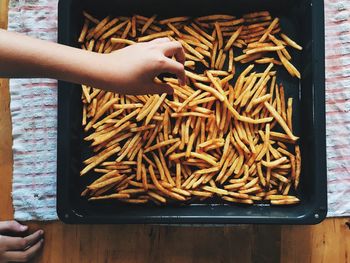 Cropped image of woman picking french fries from container on table