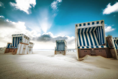 Hooded chairs on beach against sky