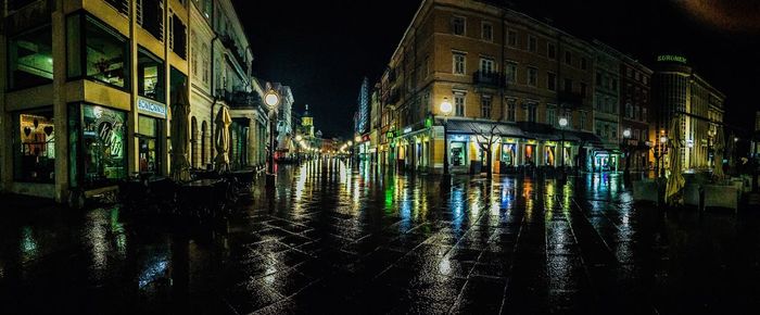 Wet street by illuminated buildings during rainy season at night