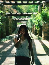 Portrait of young woman standing on footpath amidst tree