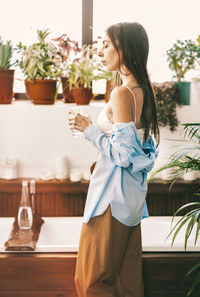 A girl with long hair, in home clothes, drinks clean water from a glass in the bathroom