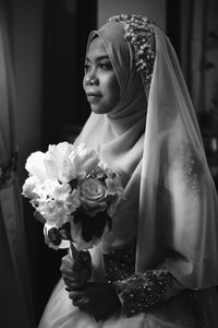 Bride wearing wedding dress holding bouquet at home