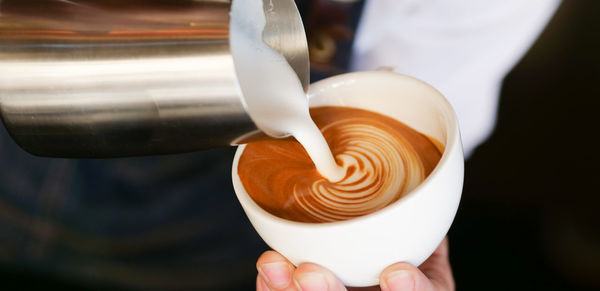 Midsection of barista pouring cream in coffee at cafe