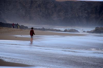 Rear view of boy walking at beach against mountains