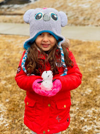 Portrait of smiling girl holding snowman standing outdoors