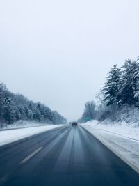 Road amidst trees against clear sky during winter