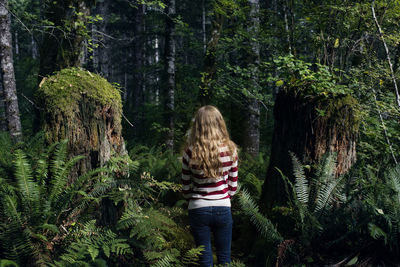 Rear view of woman standing amidst trees in forest