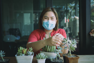 Portrait of woman wearing mask sitting by potted plant
