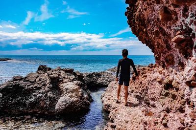 Man walking on rock at beach against blue sky