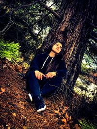 Portrait of young woman sitting on tree trunk in forest