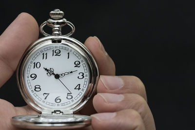 Close-up of hand holding pocket watch against black background