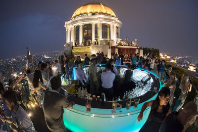 Crowd enjoying party on terrace at night against sky