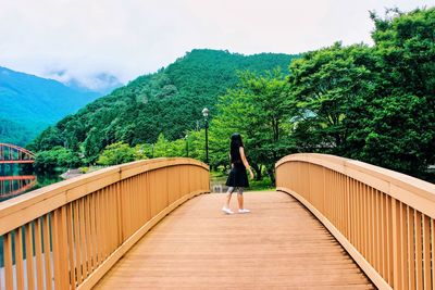 Rear view of woman walking on wooden footbridge against mountain